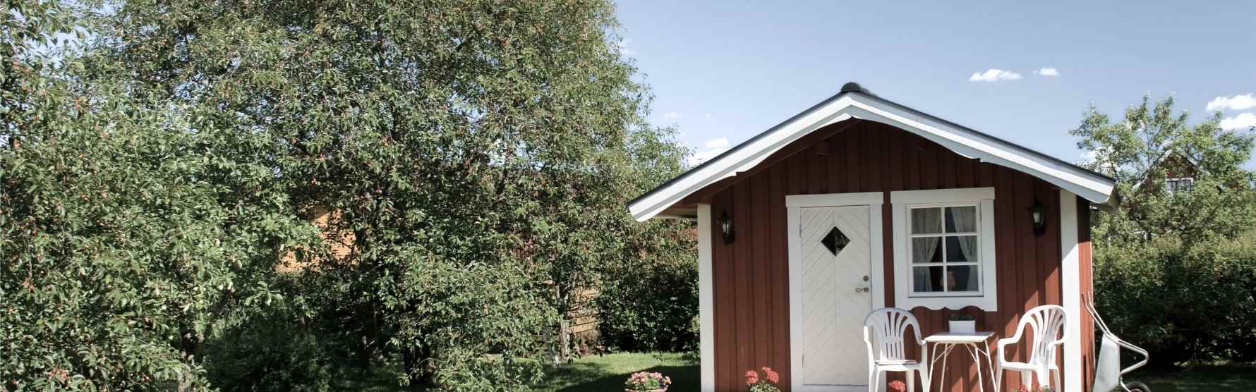 Litet rött fritidshus jämte ett stort träd