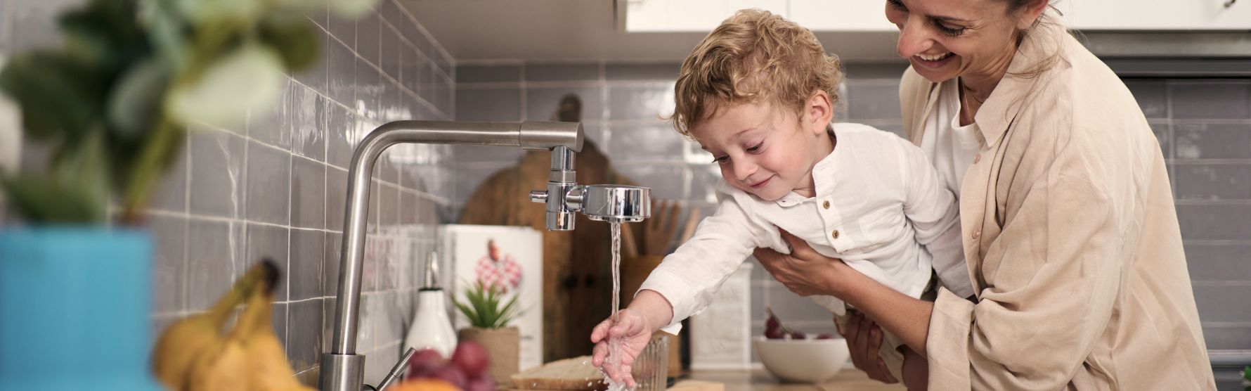 Mamma håller barn över vattenkran med kranfilter på i köket