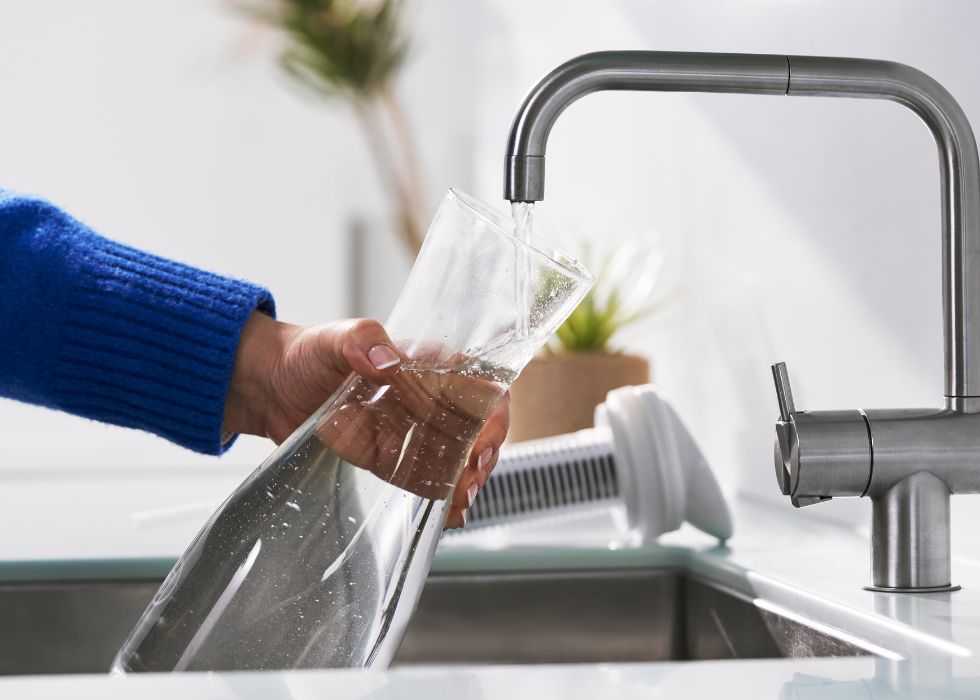 en arm som håller en filterkanna under vattenkranen med porlande vatten i ett rent kök