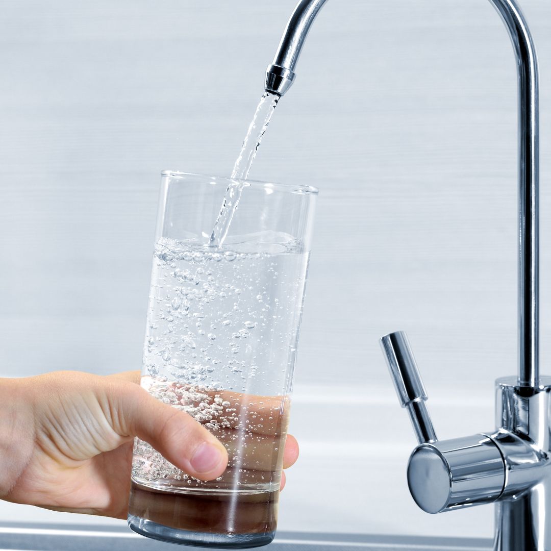 rent vatten porlar från kranen i vattenglas, hand håller glaset