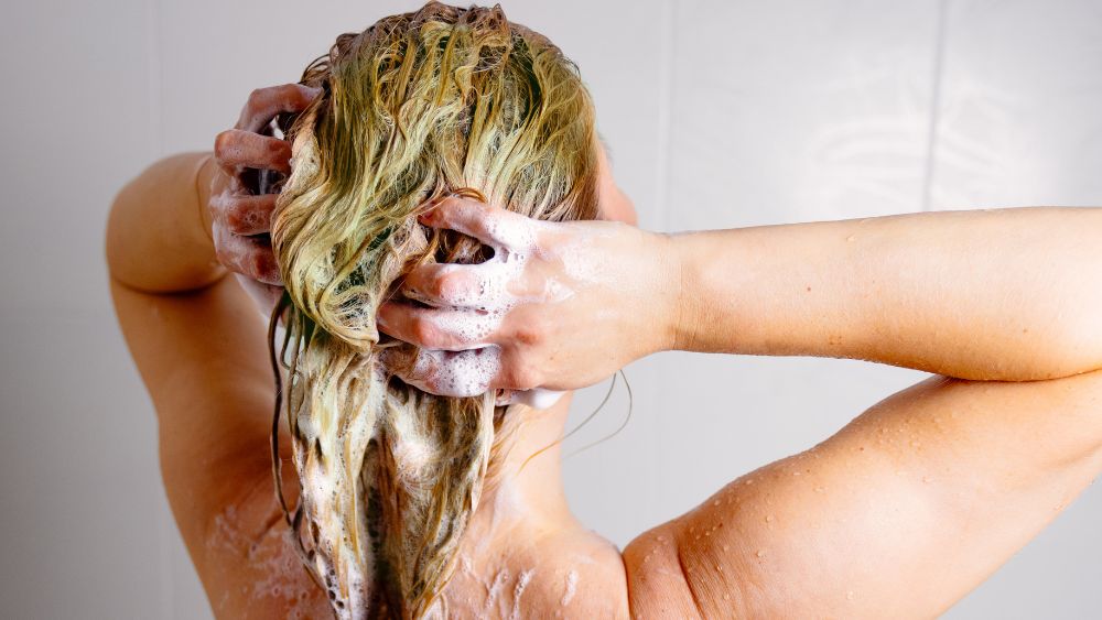 Kvinnas huvud i duschen shamponeras och har en grön nyans